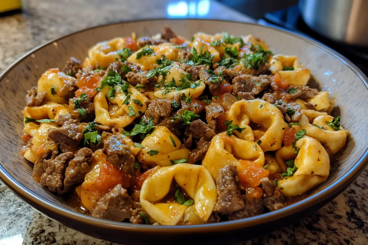 A bowl of tortellini pasta mixed with beef and tomato sauce, topped with chopped parsley.